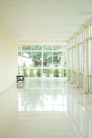 Empty walkway in building hall perspective with long white wall and long windows with light at...
