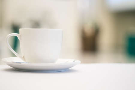 Close up white cup of coffee placed on white table with blurred people have seminar in meeting room background.の写真素材