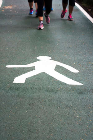 Close up white painting walking sign or icon on green lane with people walking and jogging for exercise on road in park.の写真素材