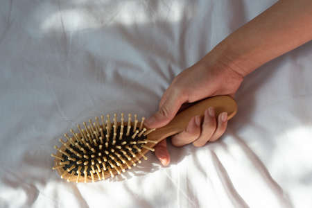 Hair fall, Hair loss problem. Woman hand holding comb with hair loss on white bed cover. Healthy and beauty concept.の写真素材