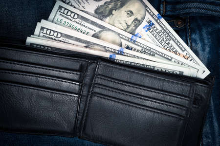 Money in black leather wallet with empty credit card slots placed on blue jean background with copy...