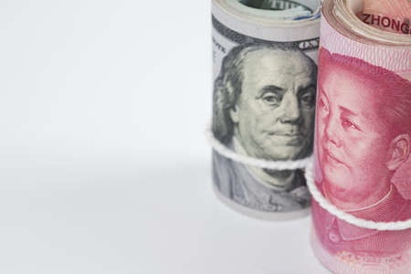 Closeup rolls of one hundred US dollar bills and chinese yuan banknotes with white robe band...