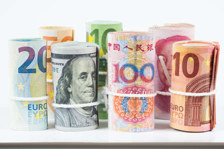 Currencies and money exchange trading concepts. The rolls of various currencies US Dollar, Euro and Chinese yuan banknotes with white rope band isolated on white background.の写真素材