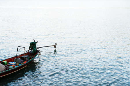 Long tail fishing boat on calm blue sea with sunlight shining on water surface.の写真素材