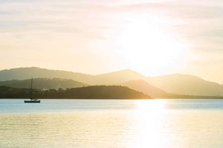 Beautiful sunset over sea and tropical beach in summer time with boat transport traveler and mountain behind. Natural background of sunset dawn and sunrise with bright dramatic scenic sky.の写真素材