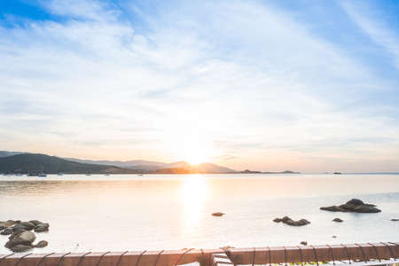 Colorful of dramatic sunset and sunrise with twilight orange sun blazing and blue sky with mountain and calm tropical sea. Summer beach background view from beach front hotel and restaurant.の写真素材