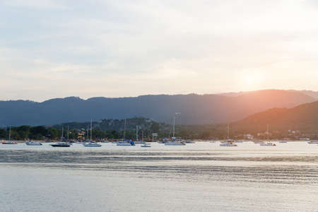 Beautiful sunset with mountain and speed boat, yacht at pier over horizon clam summer sea background evening. Scenic seascape with golden light in tropical summer beach in Koh Samui island, Thailand.の写真素材