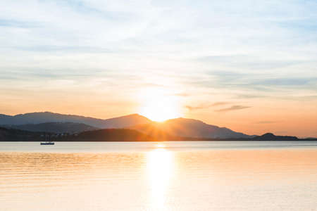 Beautiful sunrise and sunset with blue clouds over horizon clam blue sea and mountain background in morning and evening. Scenic seascape with golden light in summer.の写真素材