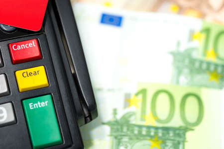 Close up of botton on credit card machine with the red credit card on top with euro banknote background and copy space. Concept of choice "enter" into be debt or "clear" and "cancel" to be debt free.  の写真素材