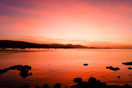 Beautiful blazing sunset landscape at black sea and mountain above orange sky with awesome sun golden reflection on calm sea as a background. Amazing summer sunset view on the beach.の写真素材