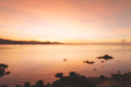 Blurred of beautiful blazing sunset landscape at black sea and mountain above orange sky with awesome sun golden reflection on calm sea as a background. Amazing summer sunset view on the beach.の写真素材