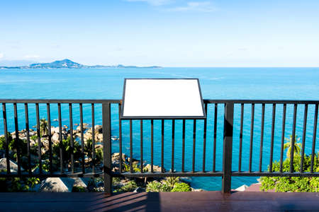 Blank advertising billboard on steel fence over calm blue sea and sky background at tropical island. Outdoor sign panel can advertisement for display, guide map, food menu and travel information.の写真素材