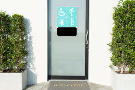 Close up toilet door with sign of disabled people, elderly, pregnant woman, and baby for their with welcome doormat and plant by the side.の写真素材