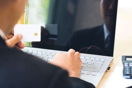 Businessman hand holding credit card and using laptop on desk with document and calculator. Man hand use card for online shopping and online payment cashless society concept.の写真素材