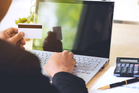 Businessman hand holding credit card and using laptop on desk with document and calculator. Man hand use card for online shopping and online payment cashless society concept.の写真素材