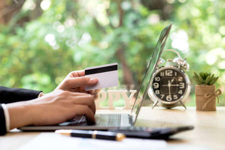 Businessman hand holding credit card and using laptop on desk with document and calculator. Man hand use card for online shopping and online payment cashless society concept.の写真素材