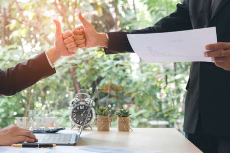 The concept of teamwork. Success businessman partners making fist bump and thump up showing trust in team after achieving goals in office with laptop, document on desk. Colleagues collaboration.の写真素材