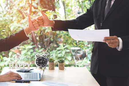 Teamwork and partner concept. Success businessman partners making fist bump and thumbs up showing trust in team after achieving goals in office with laptop, document on desk. Colleagues collaboration.の写真素材