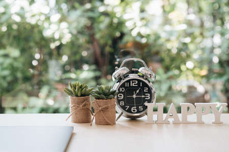 Break time concept. Happy hour time to break for employees having lunch with closing laptop, clock, small plant pots and happy word on desk in office with garden view.の写真素材