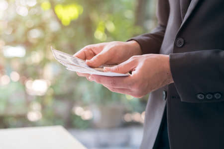 Happy and successful businessman holding US dollar money bills in hand. Close up  hand showing and counting cash in concept of investment, success, freedom, financial prospects, career advancement.の写真素材