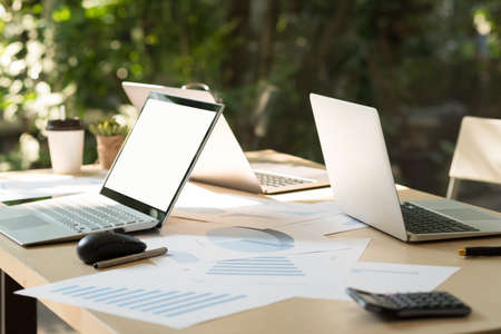 Laptop with blank white desktop screen on table with computer notebooks, business document, calculator, pen and cup of coffee in nobody office. Mockup and break time in lunch concept.の写真素材