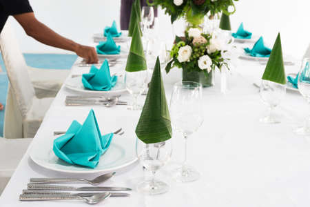 People are arranging table set with beautiful flowers and color napkin placed on white plate for dining, festive event or wedding.の写真素材