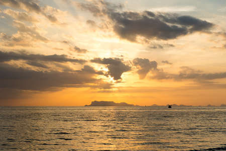 Beautiful summer sunset over the sea with sunbeam through clouds above mountain and fishing boat.の写真素材