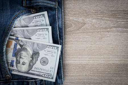 Money in pocket of blue jean on wooden background with copy space. One hundred dollar bills in back of jean pocket.の写真素材