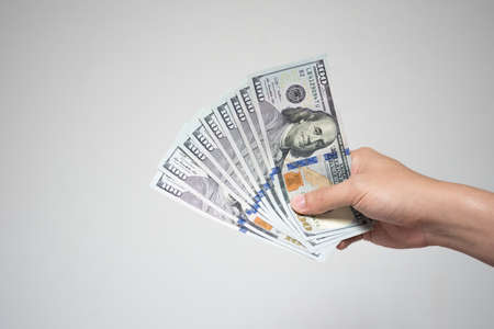 US dollar bills money in hand on white background. Close up businessman hand holding or giving many one hundred dollar banknotes in financial or donation concept.の写真素材