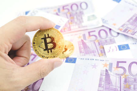 Close up man hand holding golden bitcoin over blurred five hundred euro banknotes background. Cryptocurrency, digital currency with euro money bills.の写真素材