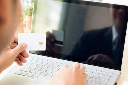 Businessman hand holding credit card and using laptop on desk with document and calculator. Man hand use card for online shopping and online payment cashless society concept.の写真素材