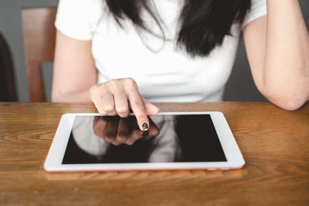 Close up woman hand and finger touching on blank digital tablet display screen on wooden table at office. Young businesswoman searching browsing information on internet. Internet of things (IoT)の写真素材