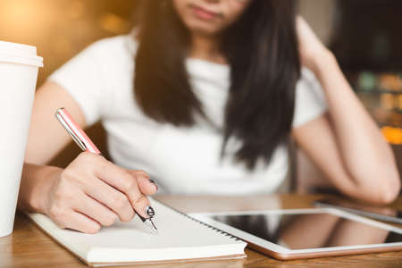 Close up hand of happy smile college student woman with pink pen writing down ideas on notebook...