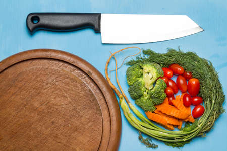 dill. baby tomatoes. carrot. broccoli. knife. on old chopping borad wooden. on wood color sky. blue. kitchen.の写真素材