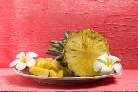 pineapple on dish half with flower on pink wood.