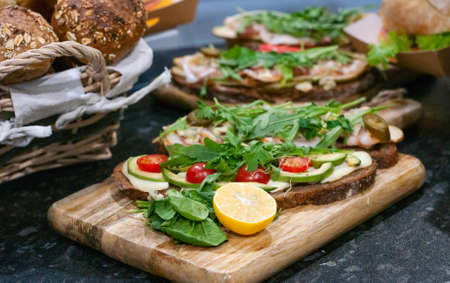 Sandwiches with tomatoes, lettuce, ham, lemon and arugula on dark bread.の写真素材
