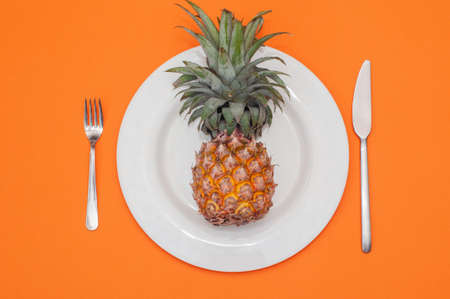 one Yellow pineapple on a white plate, flat lay, horizontal orientation, orange background.の写真素材