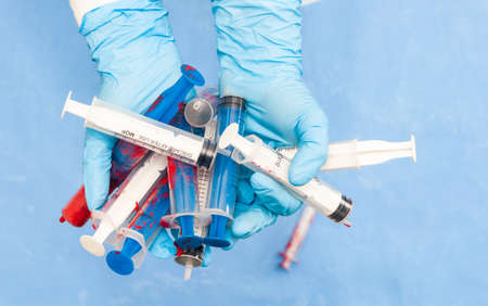 Protective medical syringe in hands on a blue background. Hands in gloves. View from above. Virus Prevention. Place for text. close upの写真素材
