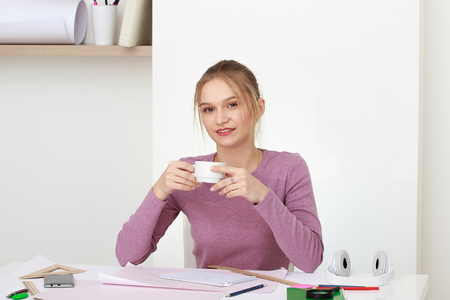 Portrait of a smiling student girl sitting at the desk with a mugの写真素材