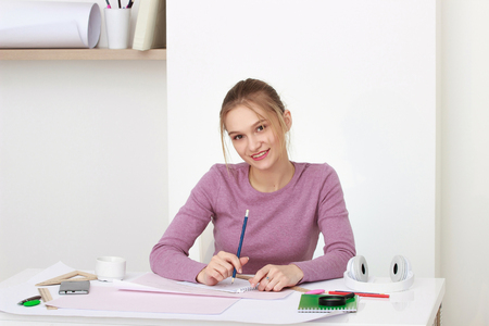 The young girl is studying while sitting at a white tableの写真素材