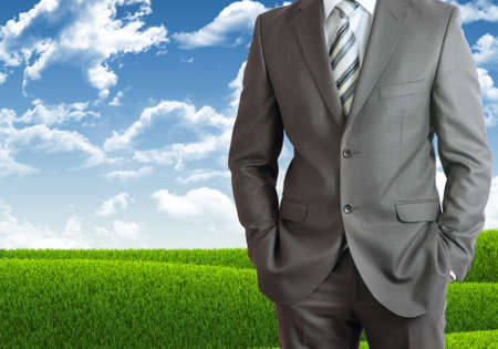 Businessman standing with hands in pockets  Blue sky and green grass as backdropの写真素材