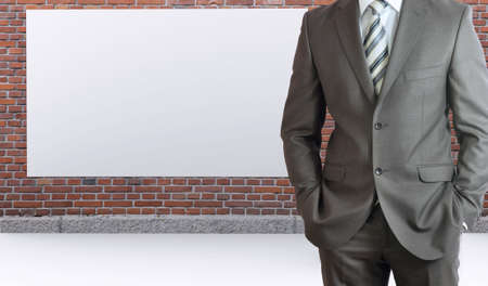 Businessman standing with hands in pockets  Brick wall and white placard as backdropの写真素材