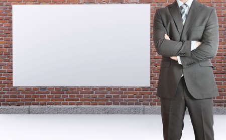 Businessman standing with his arms crossed  Brick wall and white placard as backdropの写真素材