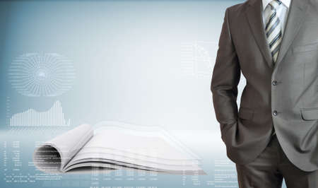 Businessman standing with hands in pockets  On background of the open book and high-tech graphsの写真素材