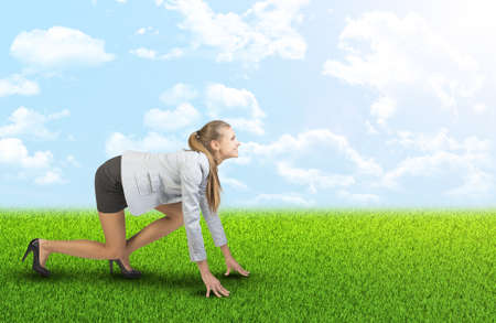 Businesswoman standing in running start pose at green field, looking ahead, smilingの写真素材