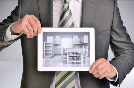 Three-dimensional model of kitchen in tablet screen. Man holding tablet in hand. Gray backgroundの写真素材