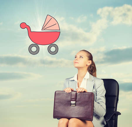 Business woman in skirt, blouse and jacket, sitting on chair imagines buggy. Against background of sky and cloudsの写真素材
