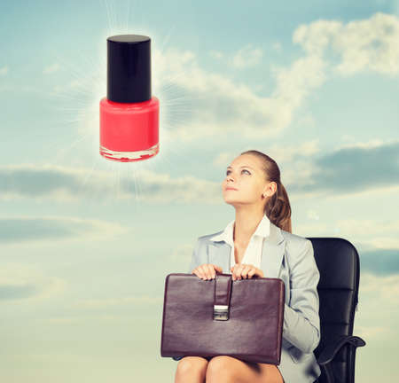 Business woman in skirt, blouse and jacket, sitting on chair imagines nail polish. Against background of sky and cloudsの写真素材