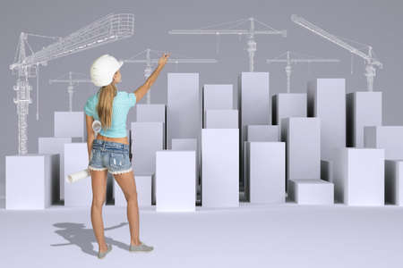 Beautiful girl in working clothes holding paper scrolls and pointing finger. Rear view. Minimalistic city of white cubes with wire-frame tower cranes on gray backgroundの写真素材