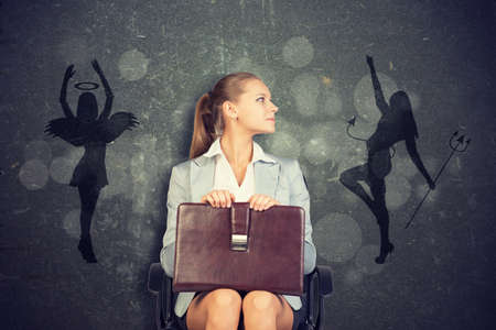 Young Businesswoman Sitting in Chair with Briefcase in Lap Looking to the Side, Framed by Silhouettes of Angel and Devil in Ethical Concept Imageの写真素材
